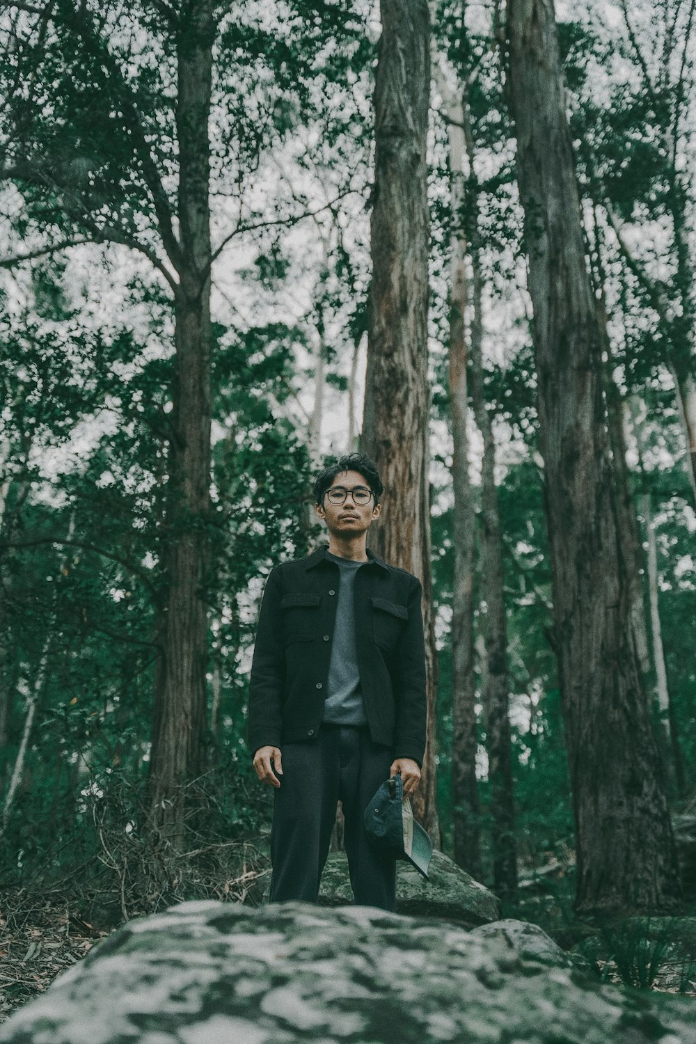 homem em casaco preto em pé no meio da floresta durante o dia