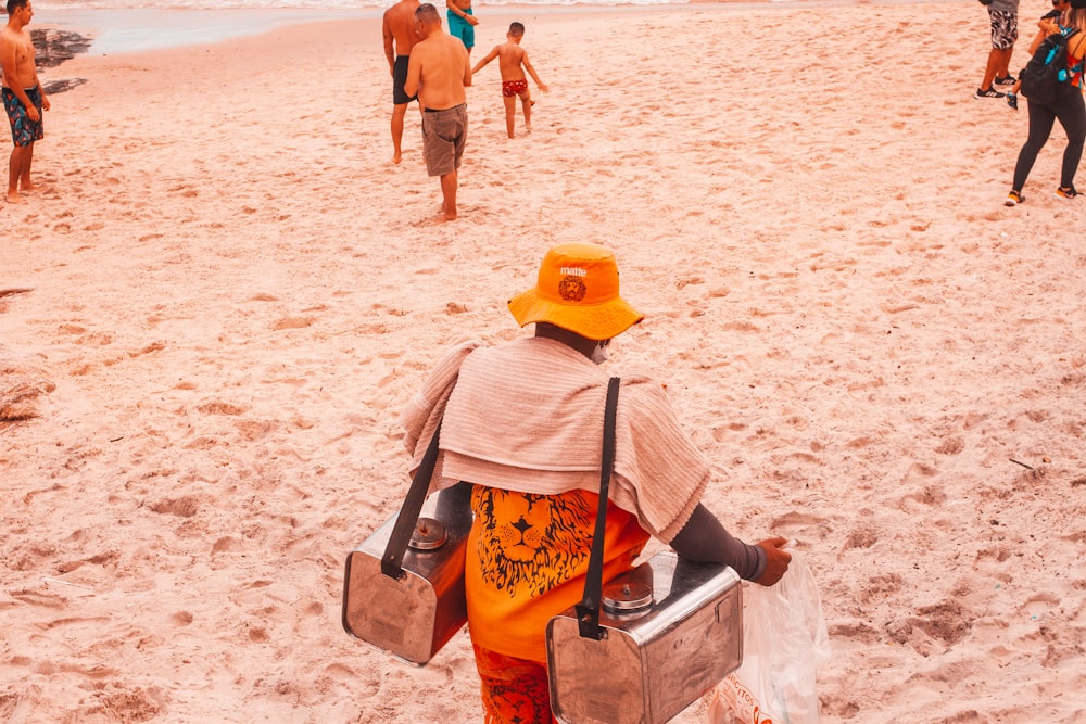 Frau mit braunem Sonnenhut und braunem Rucksack sitzt auf weißer Betonbank am Strand während