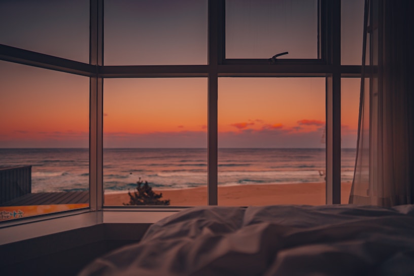 Cozy beachfront apartment with large windows showing the ocean view at sunset.