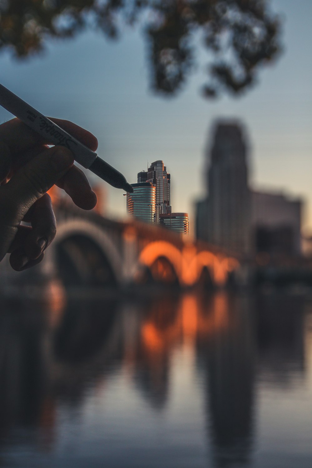 person holding black pen near body of water during sunset