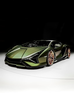 A sleek, high-performance green sports car with a modern design, aggressive aerodynamics, and copper-colored wheels posed on a well-lit, reflective surface against a dark background.