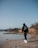man in black hoodie standing on brown field near lake during daytime