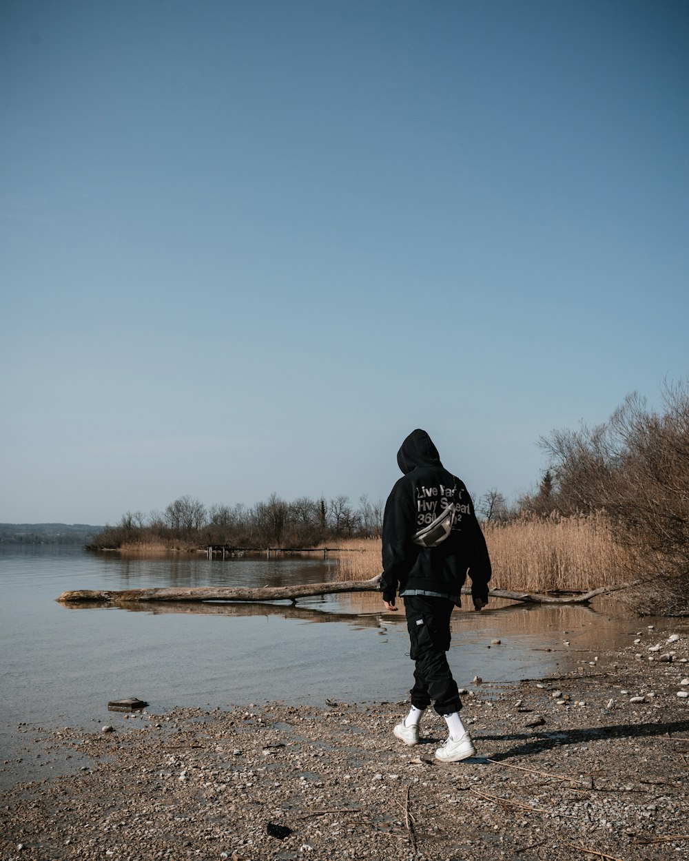 man in black jacket and pants standing on brown field near lake during daytime