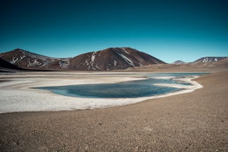 brown mountain near body of water under blue sky during daytime