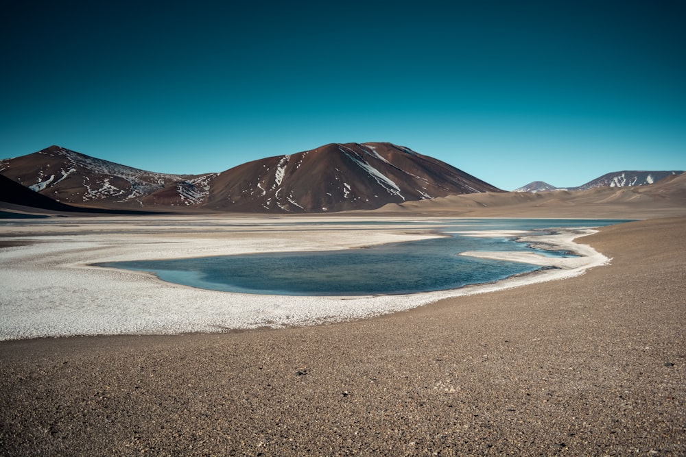 brown mountain near body of water under blue sky during daytime