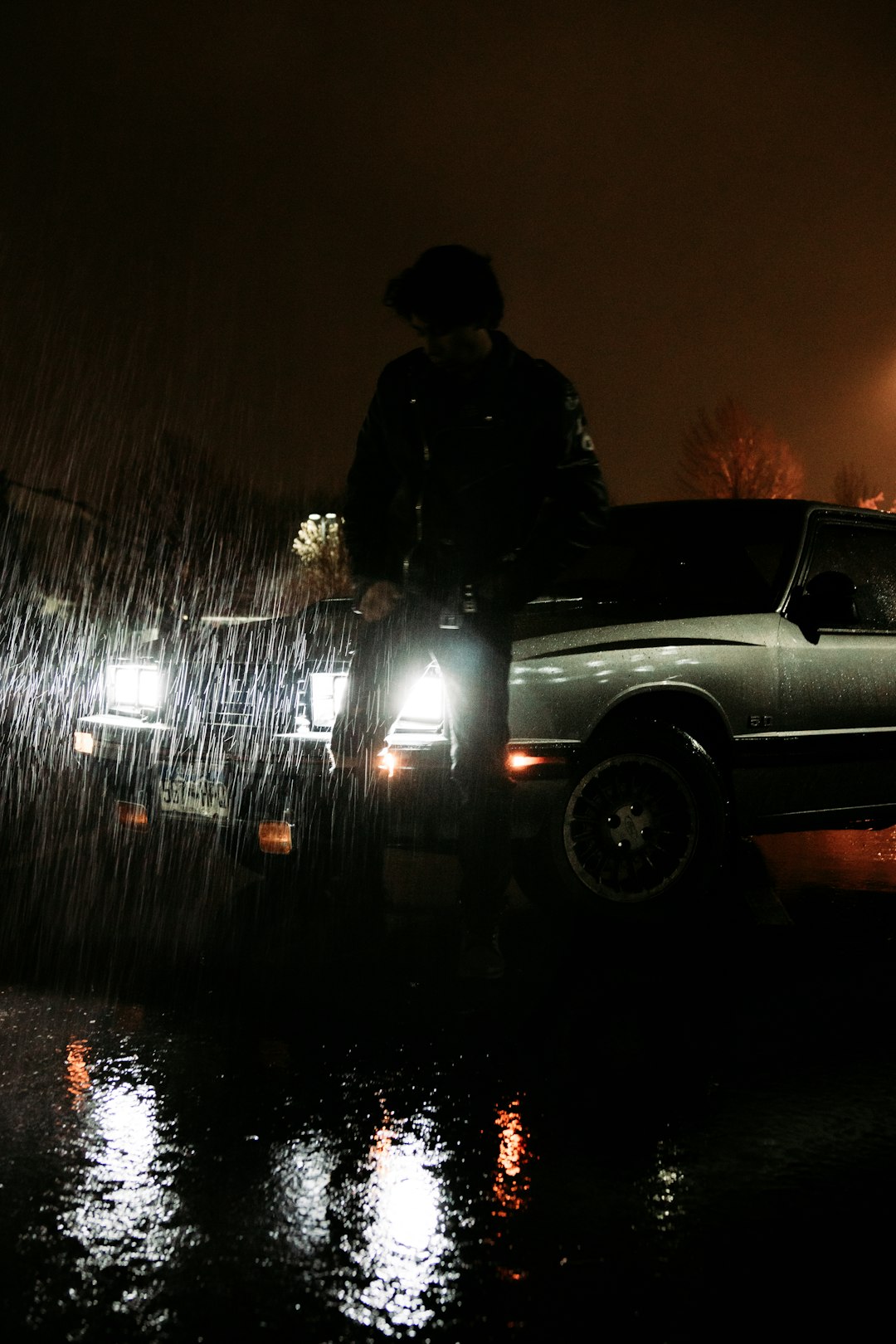 man in black jacket standing beside black car during night time