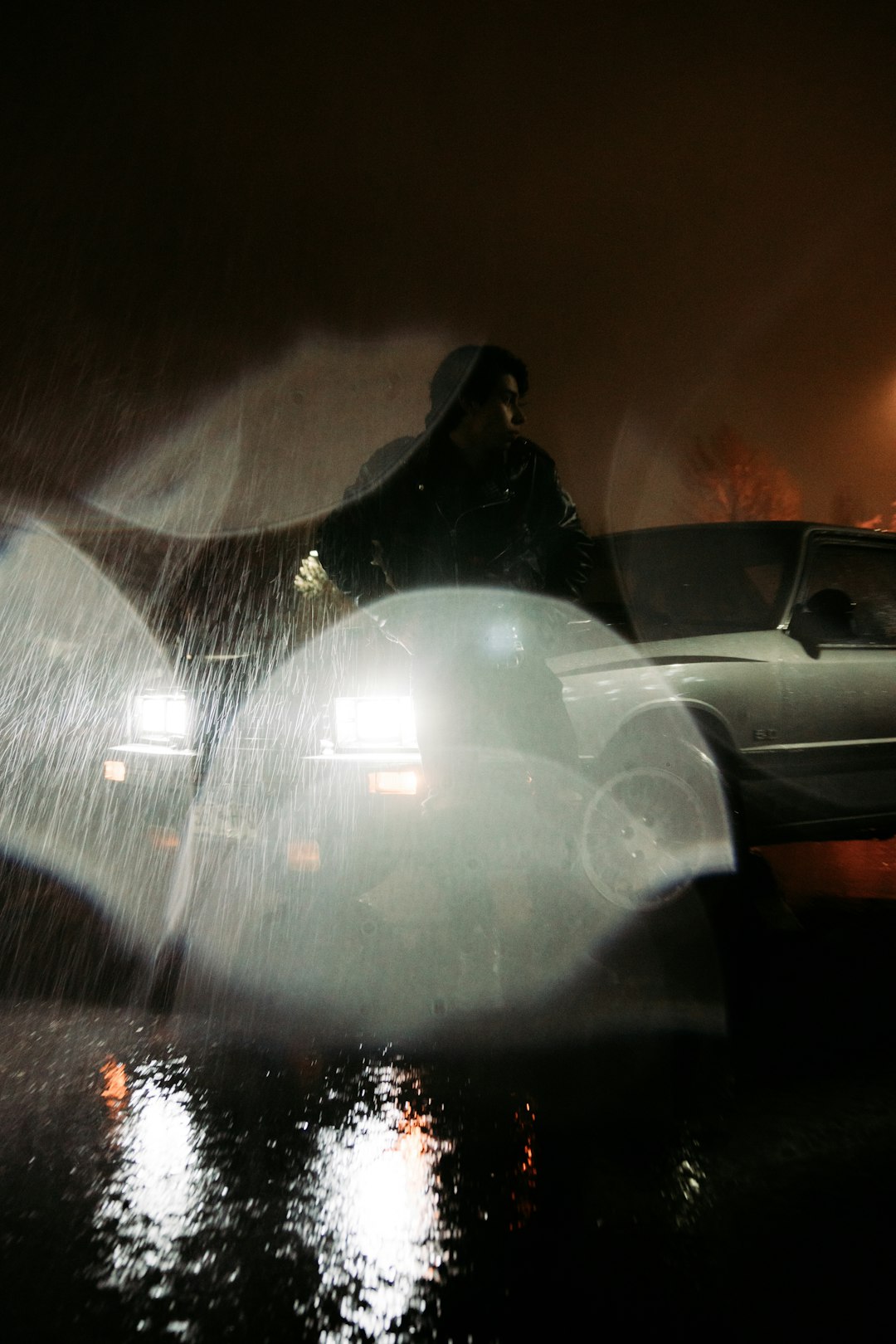 man in black jacket standing beside white car during night time