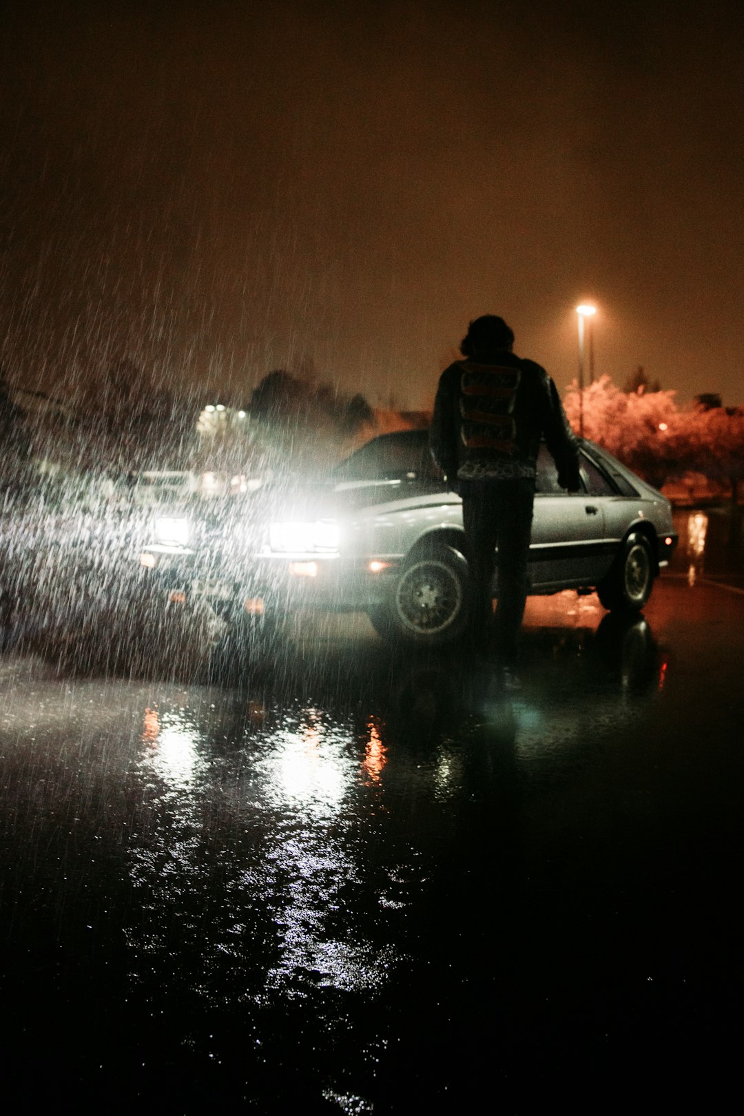 man in black jacket standing beside white suv during night time