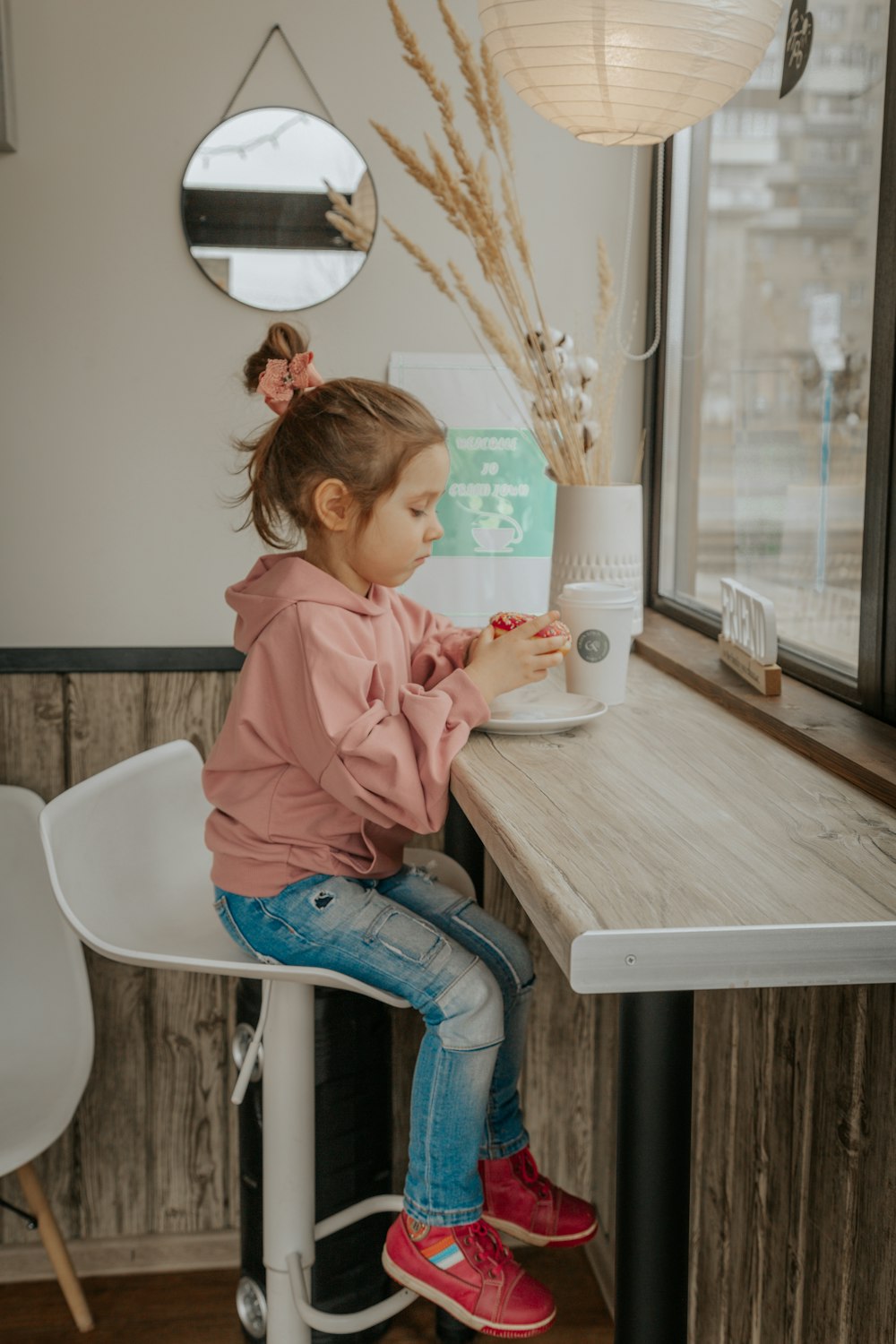 girl in pink hoodie and blue denim jeans sitting on white plastic chair