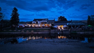 Sunset view of the outdoor riverside dining area with wooden tables and soft lighting.