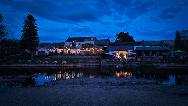 A cozy riverside café decorated with British flags and memorabilia, overlooking a calm river at sunset.
