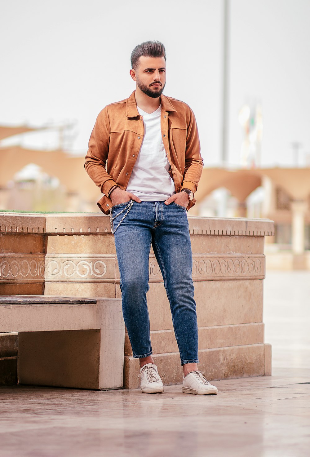 uomo in giacca marrone con cerniera e jeans blu in denim che si siede sulla panchina di cemento marrone durante