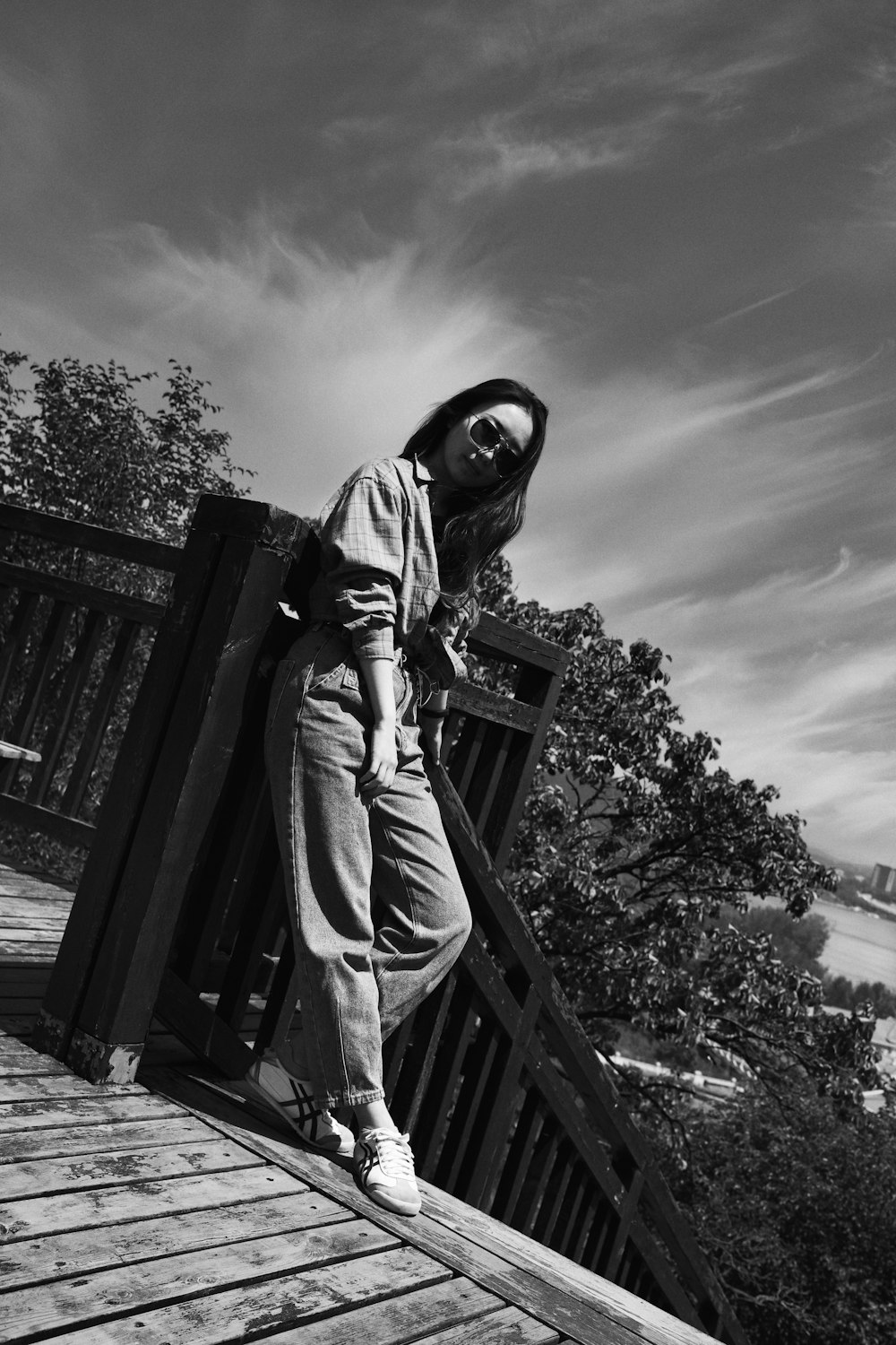 grayscale photo of person in hoodie and pants standing on wooden dock