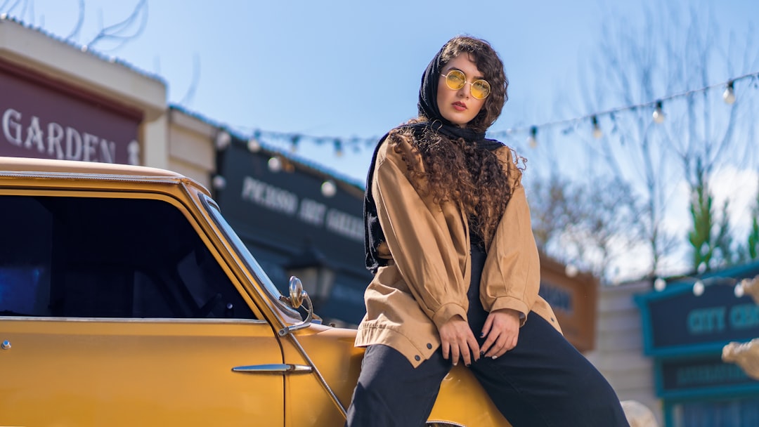 woman in brown coat and black pants sitting on yellow car