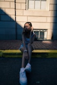 woman in black tank top and blue denim shorts sitting on gray concrete pavement