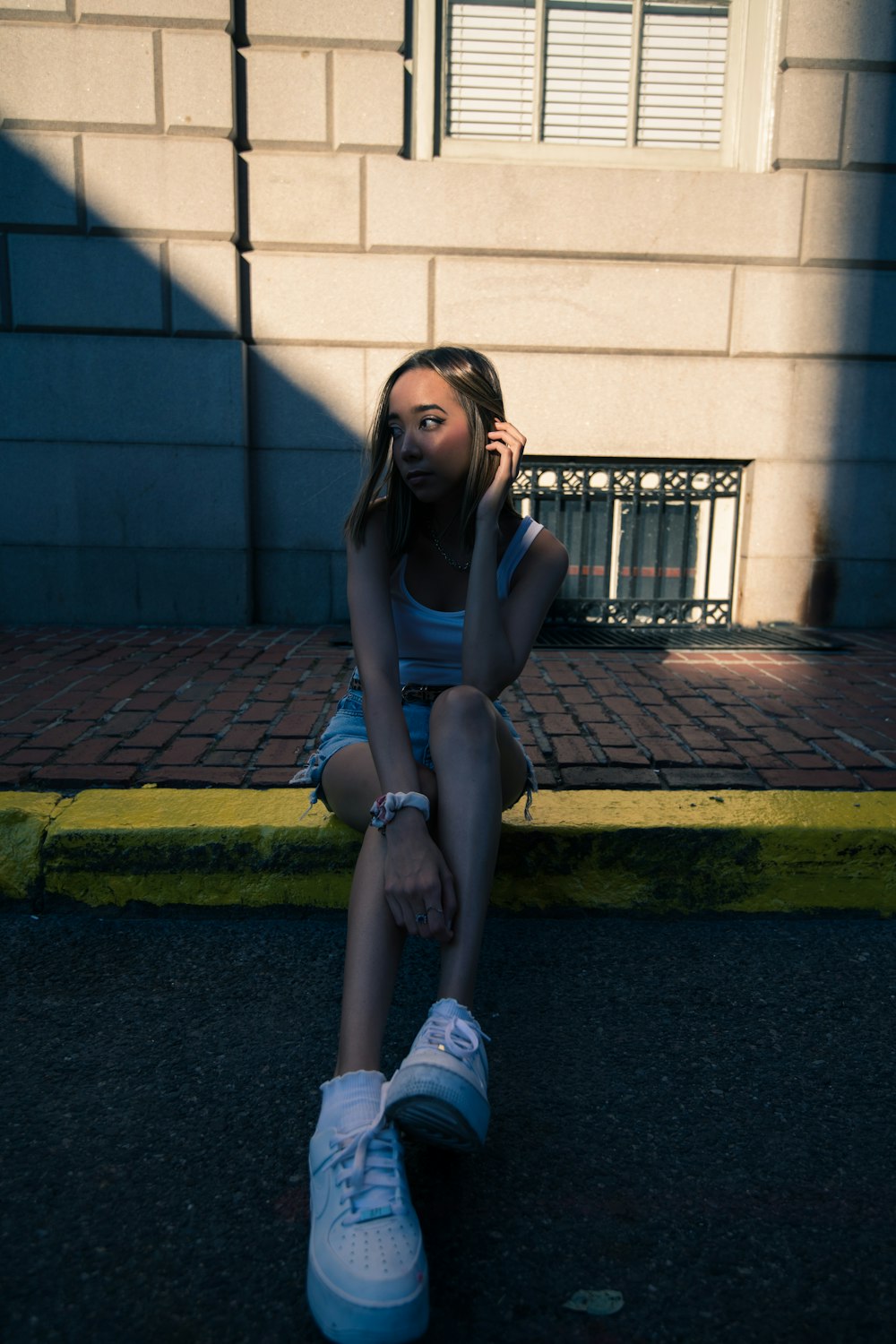 Femme en débardeur noir et short en jean bleu assise sur un trottoir en béton gris