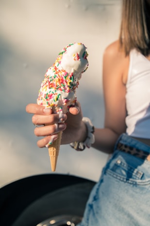 A close-up of a colorful ice cream cone with vibrant sprinkles melting slightly in the sun.