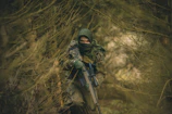 A survivalist wearing tactical gear trekking through a misty, wild forest landscape.