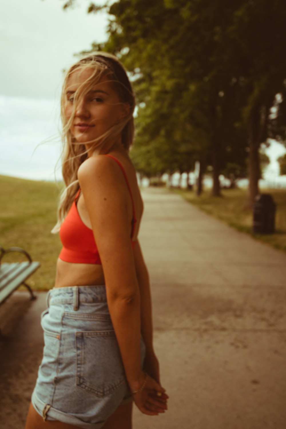 Woman in red sports bra and blue denim shorts standing on gray