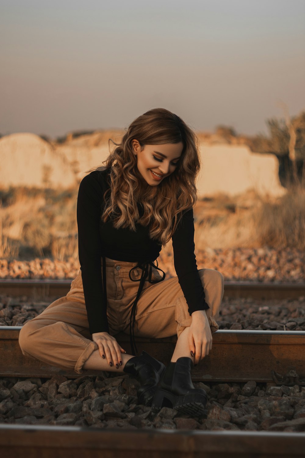 Femme en chemise noire à manches longues et pantalon marron assise sur un banc en bois marron pendant la journée