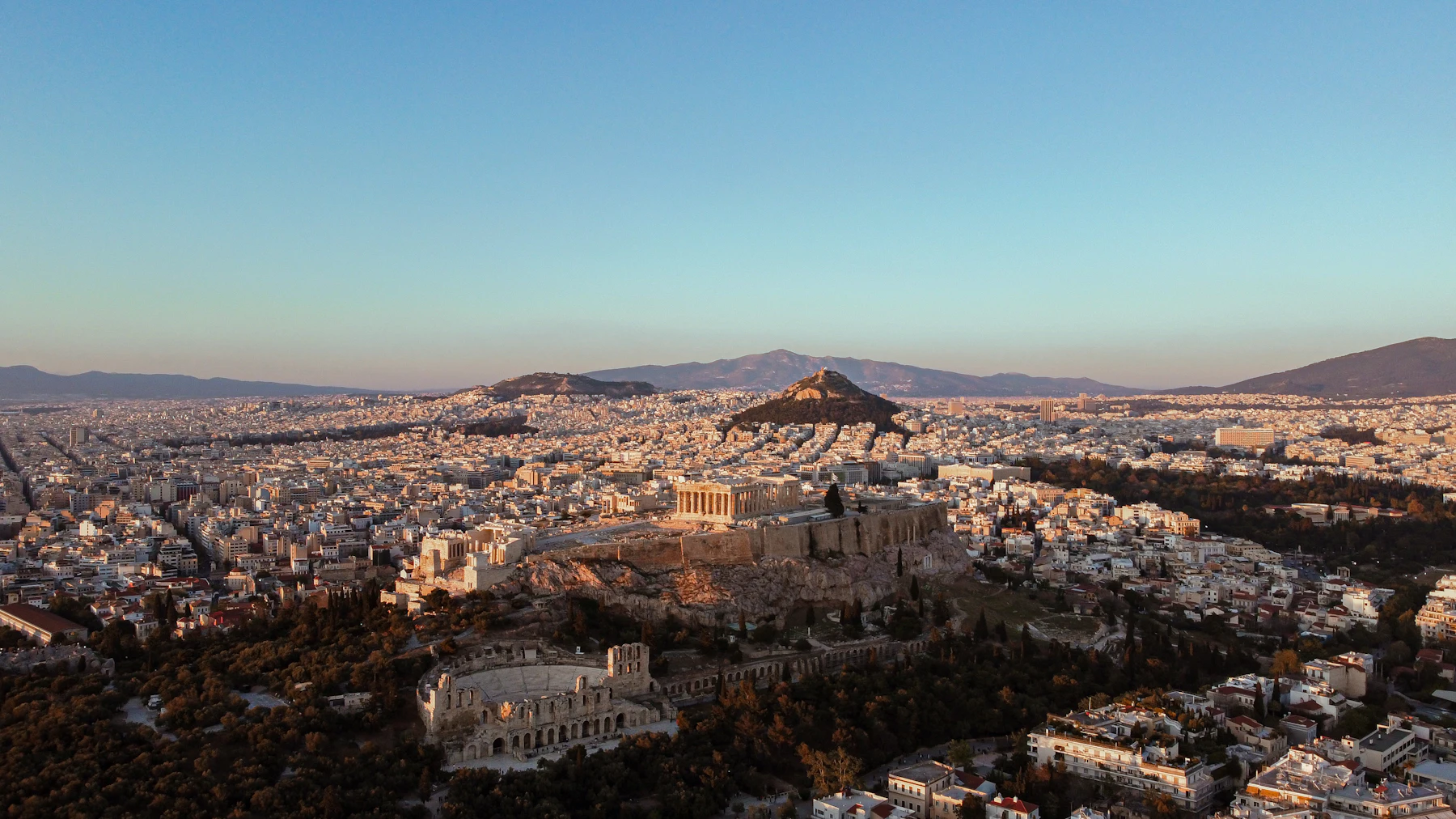 Athens from the air under low sun, the city running out to the hills.