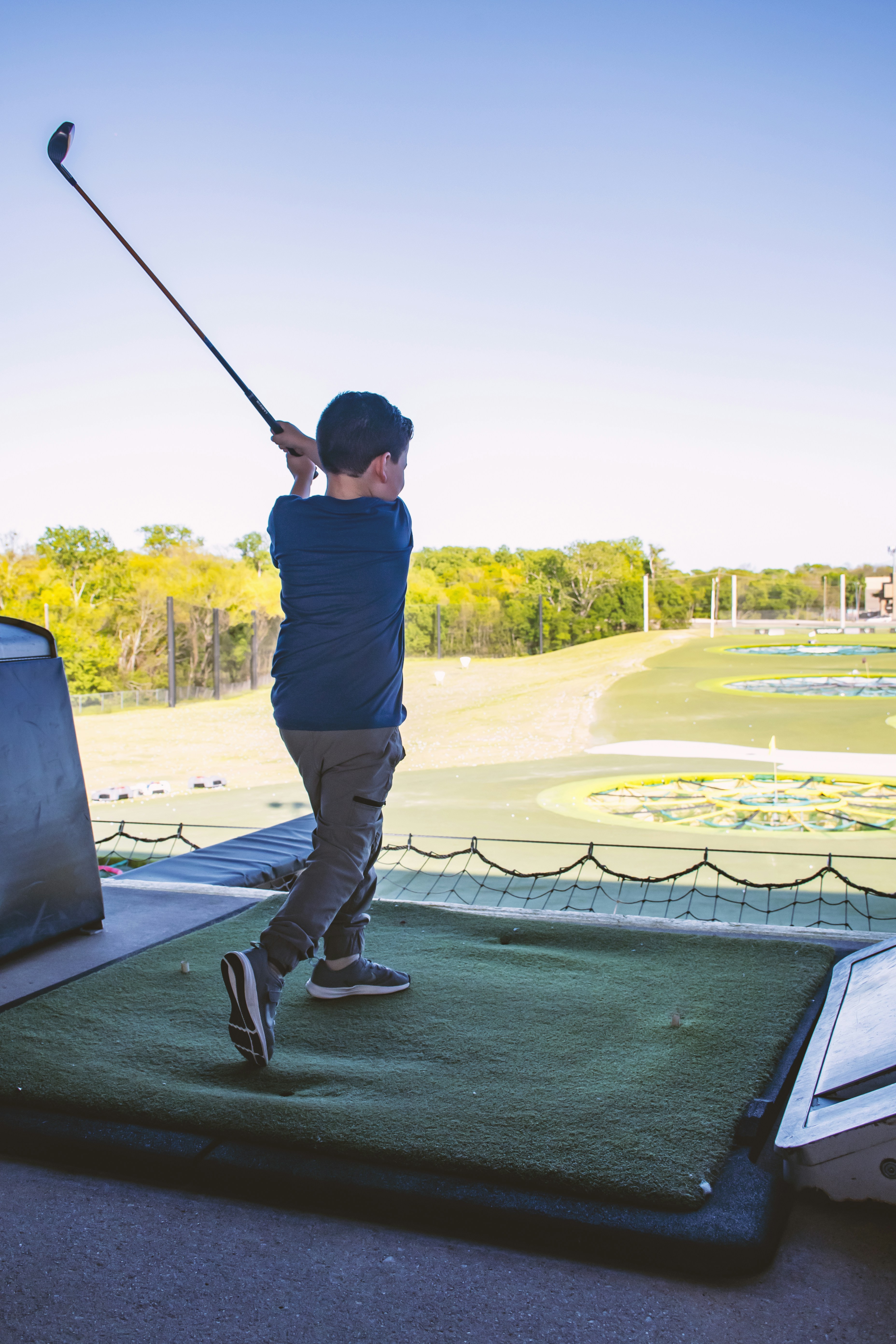 Young man teeing off at a driving range, focused expression, warm afternoon light