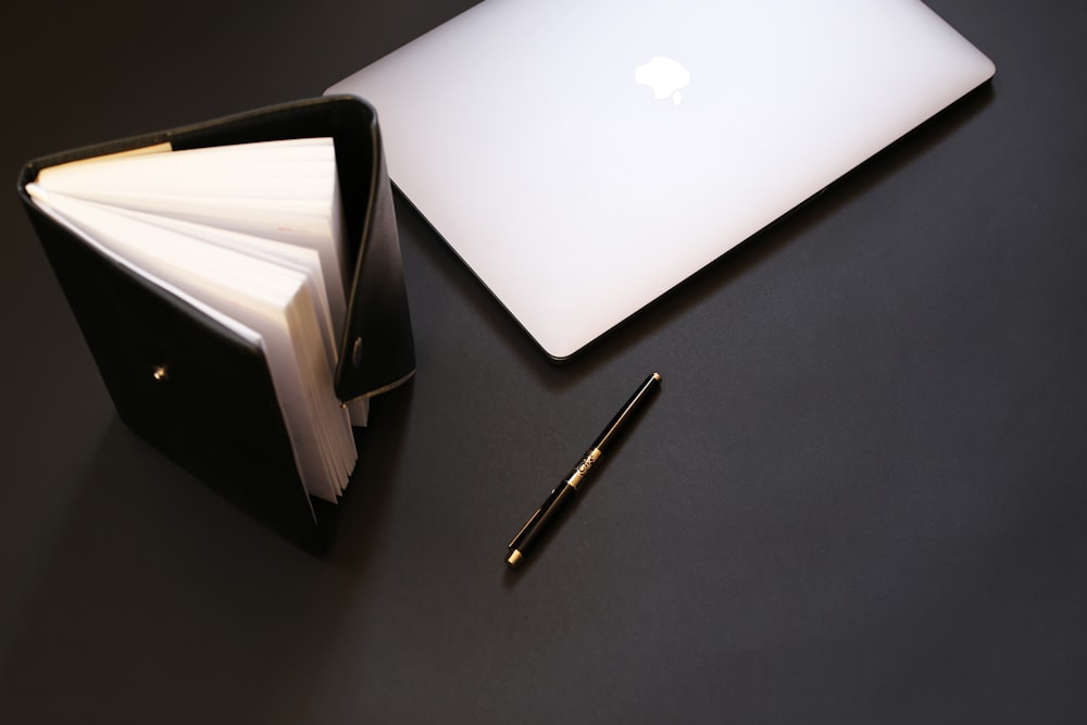 silver macbook beside black pen