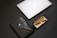 A sleek and modern composition featuring a closed silver laptop with an apple logo, a black leather portfolio with a button closure, and a black fountain pen inside an open black case with a beige interior.