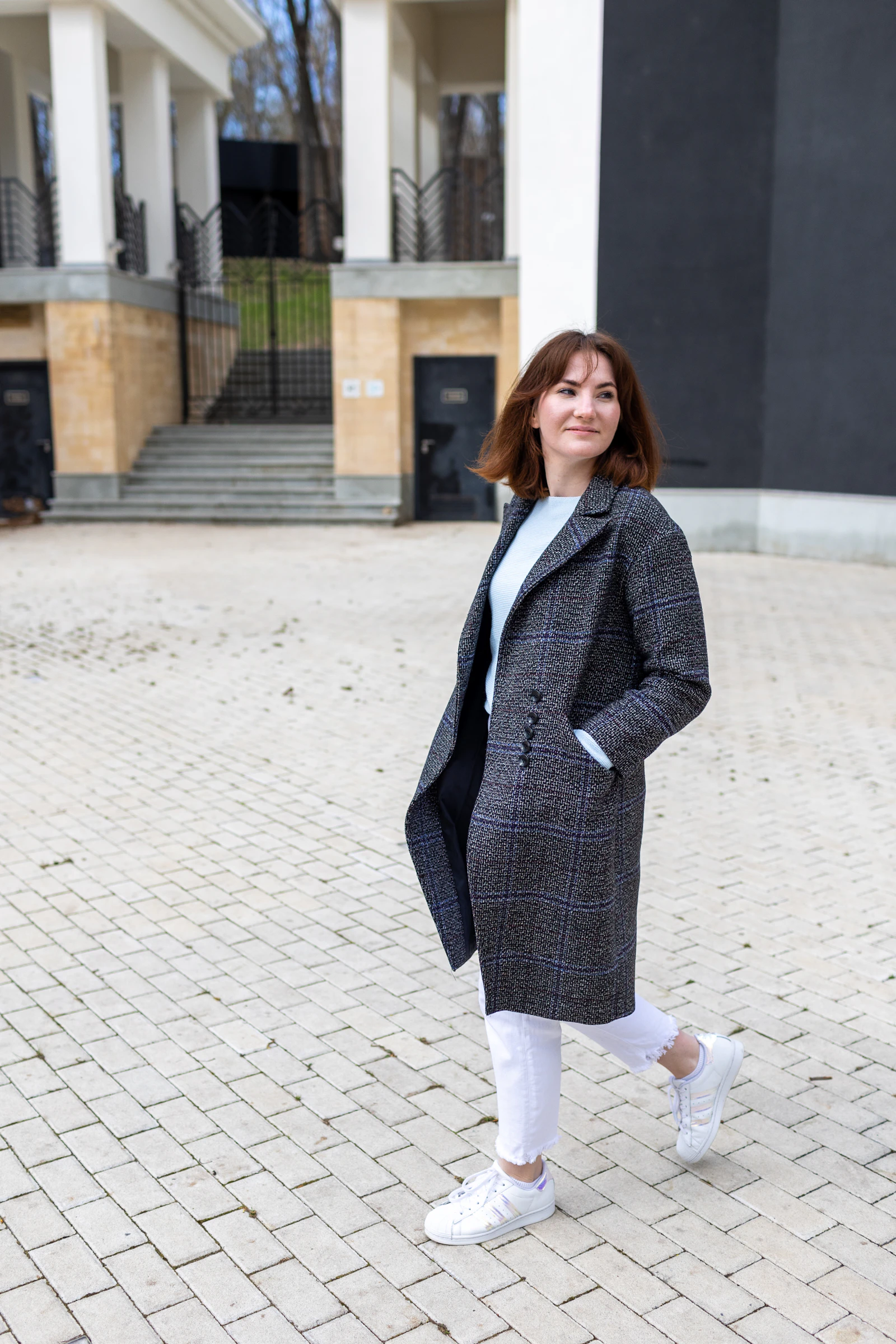 A woman in a tailored grey coat walking along a cobbled street