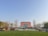 A large red brick building is seen in the center, flanked by rows of trees and a neatly manicured lawn in the foreground. Several workers in uniform are gathered near vehicles and are possibly engaging in landscaping activities. The letters 'Chengdu University' are prominently displayed on the lawn in front.