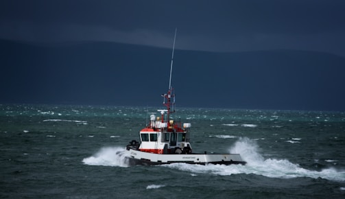 An oil tanker navigating through turbulent sea waters under dark storm clouds.