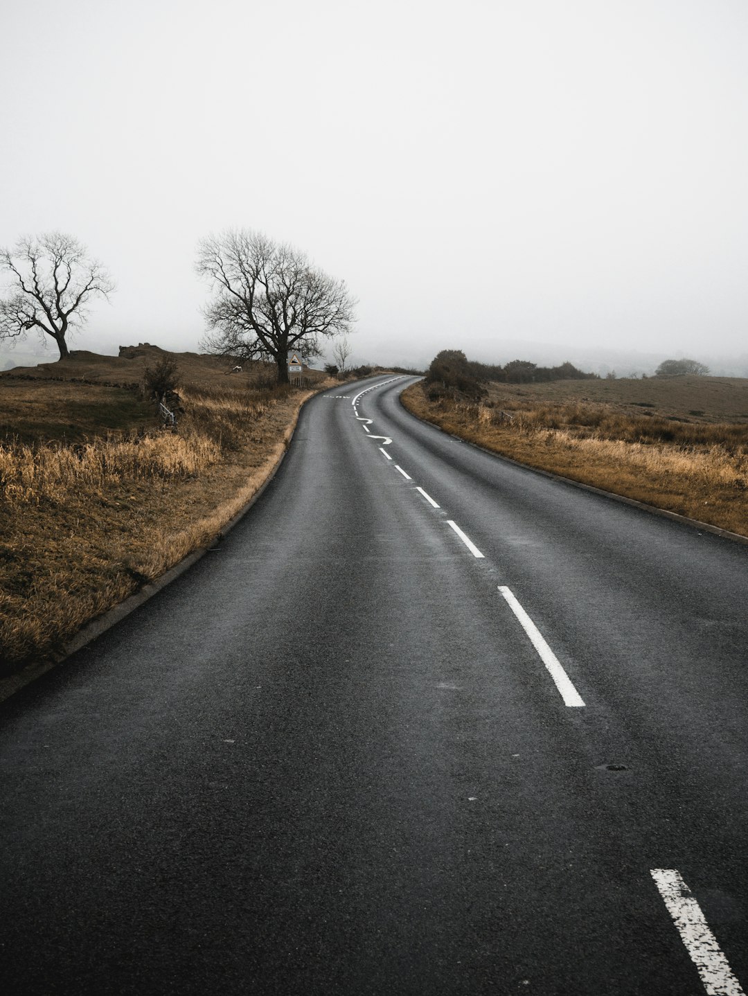 gray asphalt road between brown grass field during daytime