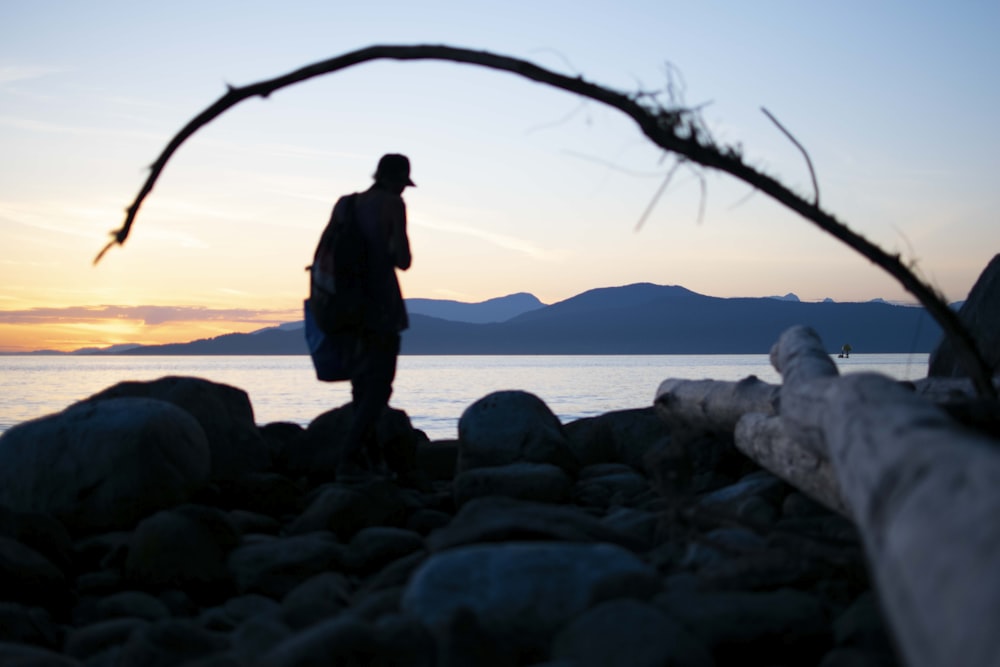 man in black jacket standing on rock near body of water during daytime