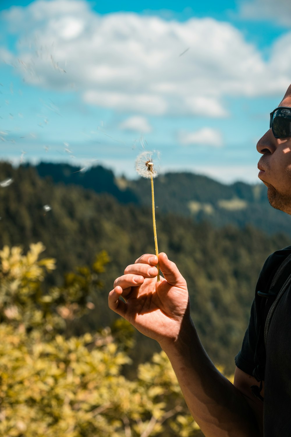 man in black jacket holding white dandelion flower during daytime