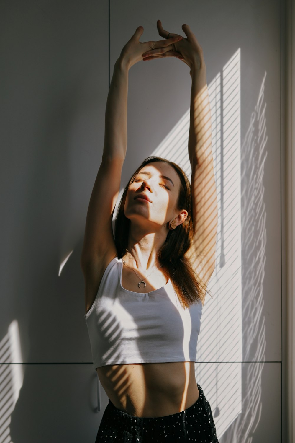 Mujer con camiseta blanca sin mangas de pie junto a la pared blanca