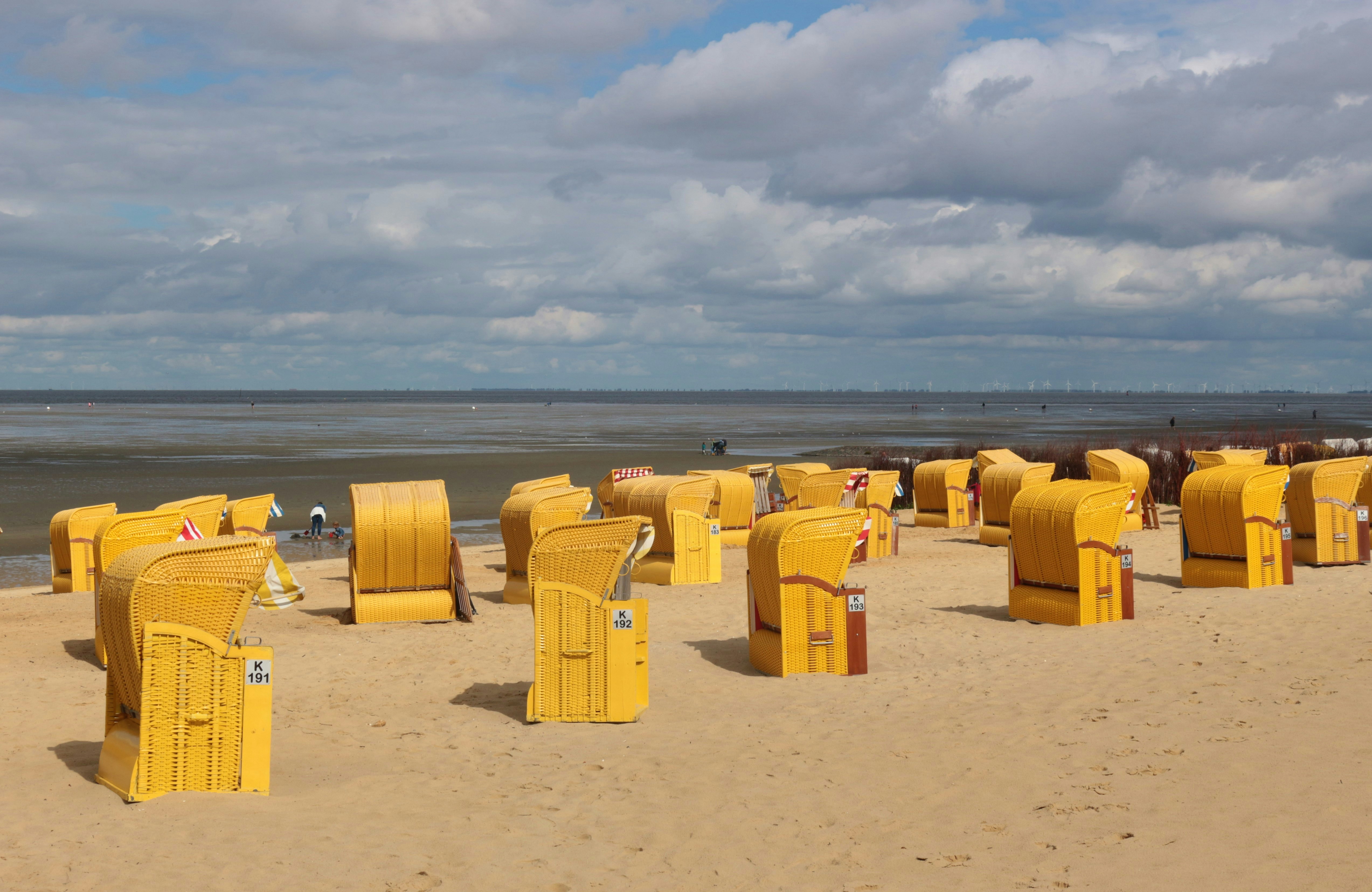 Bright yellow beach chairs on a sandy beach by the North Sea, Cuxhaven, North Germany. People walk on the wadden sea, it is low tide. Europe.