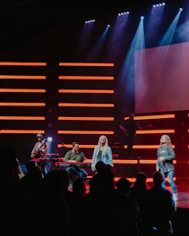 A vibrant group of young musicians performing passionately on stage under green and red lights.