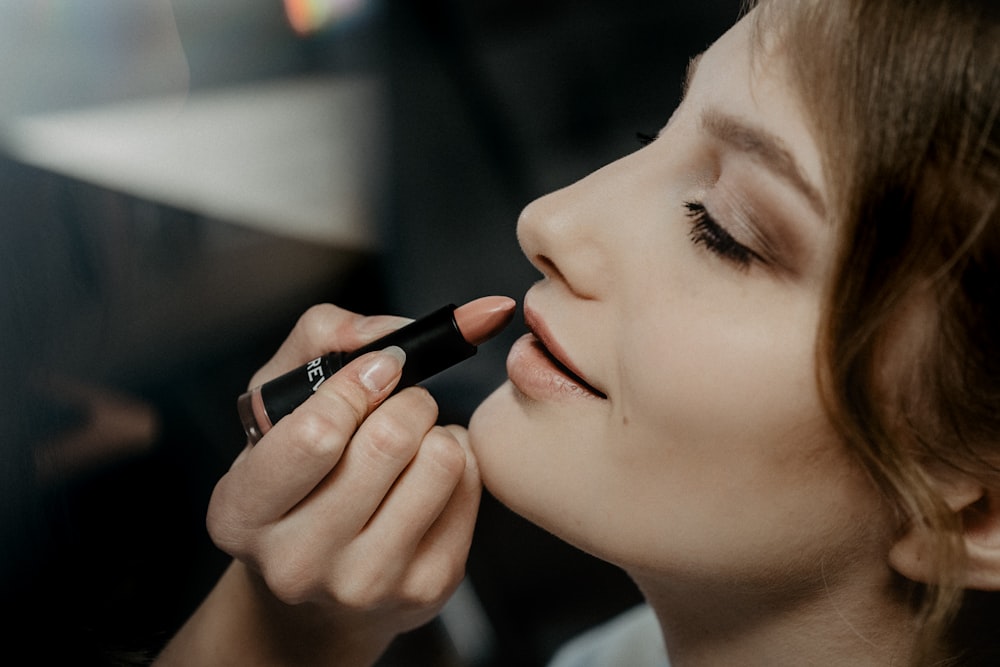 woman holding black lipstick in close up photography