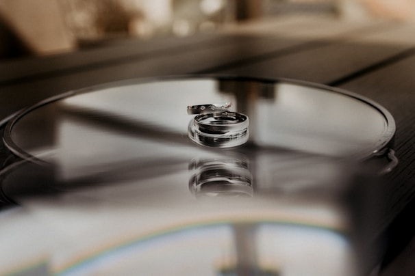 Elegant silver rings displayed on a reflective glass surface.