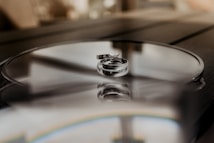 Two silver rings are elegantly placed on a reflective surface, capturing a soft and intimate atmosphere. The background is blurred, accentuating the focus on the rings and the subtle reflections they create.