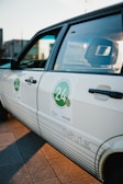 A close-up view of a white car with a sticker on the side door featuring the number 24 and some text with an automotive theme. The car has a retro design, and the sunlight creates a warm glow on the surface.