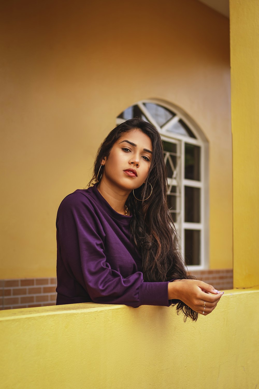 woman in purple long sleeve shirt leaning on yellow wall