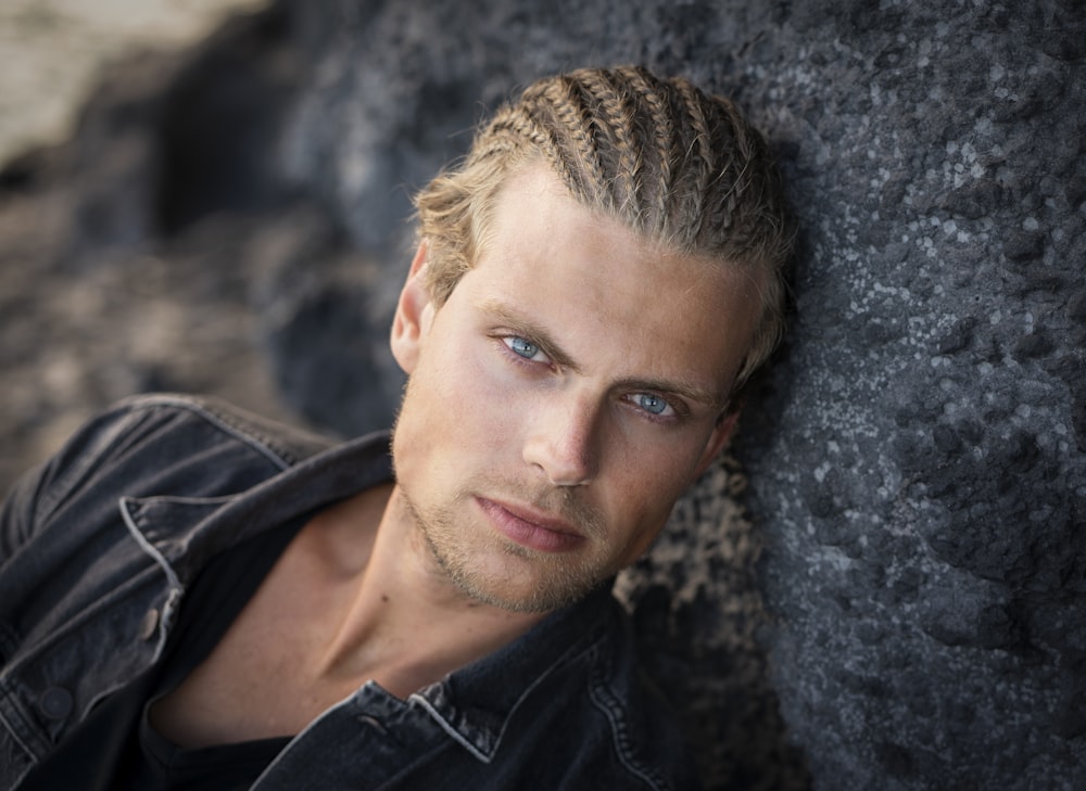 man in black leather jacket leaning on gray rock