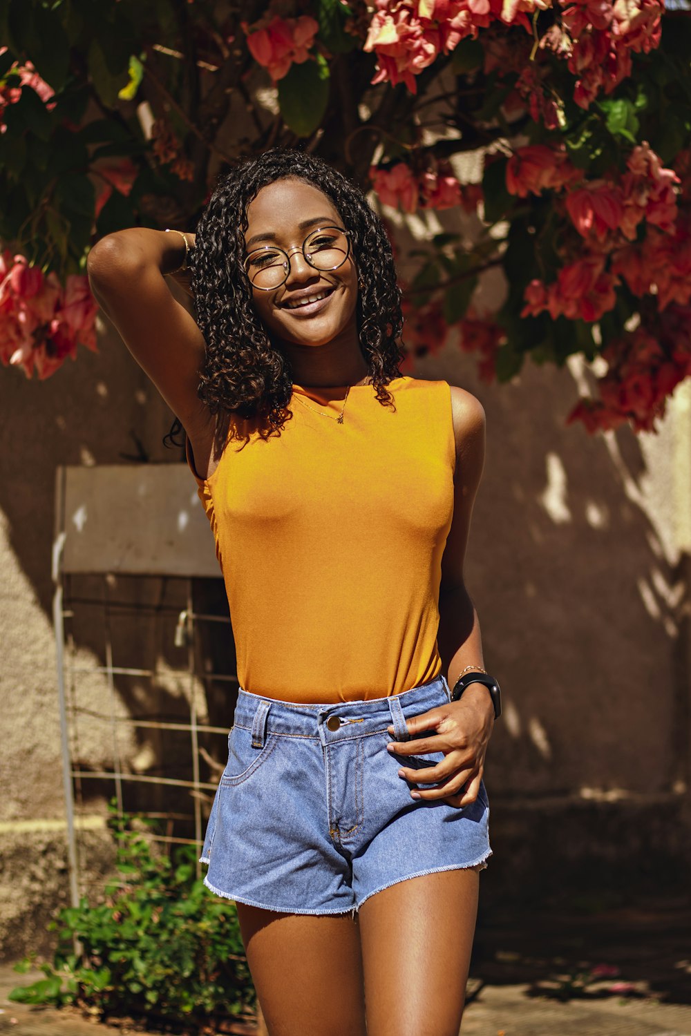 Woman in yellow tank top and blue denim shorts standing near red flowers  photo – Free Clothing Image on Unsplash