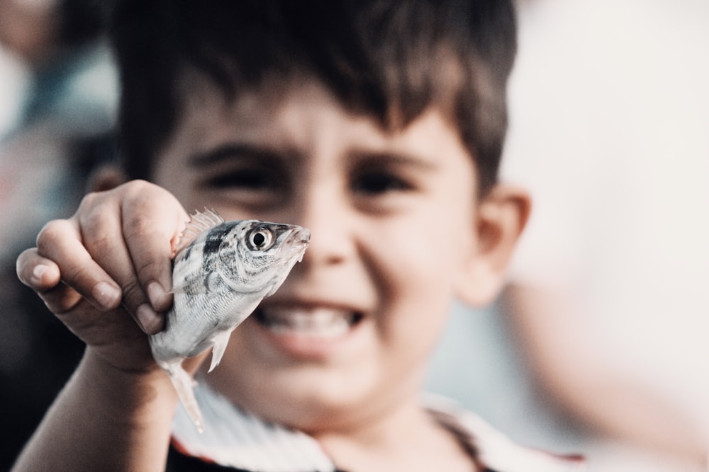 menino segurando peixe cinza e preto