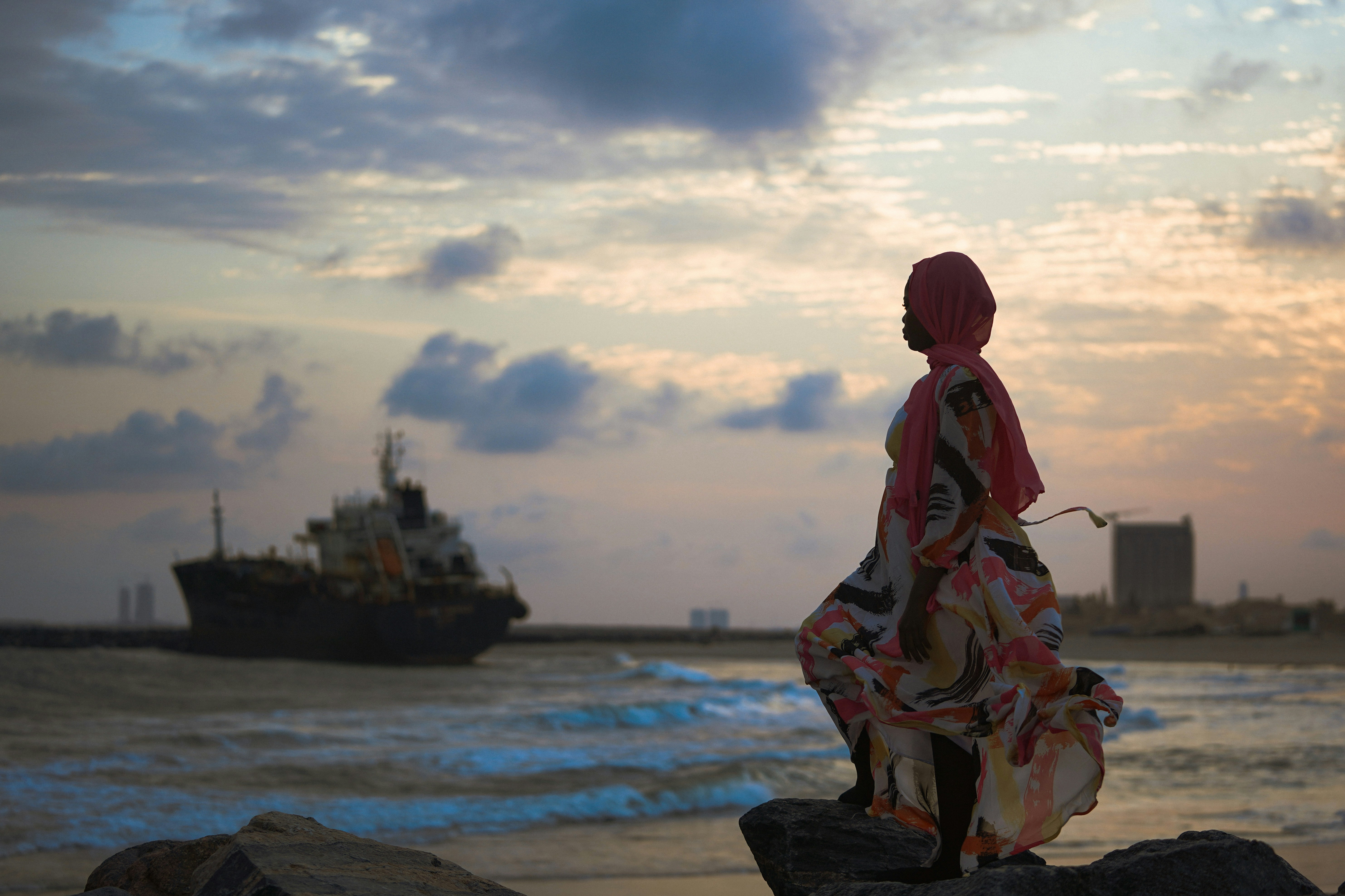 woman in red and white dress sitting on rock near sea during daytime