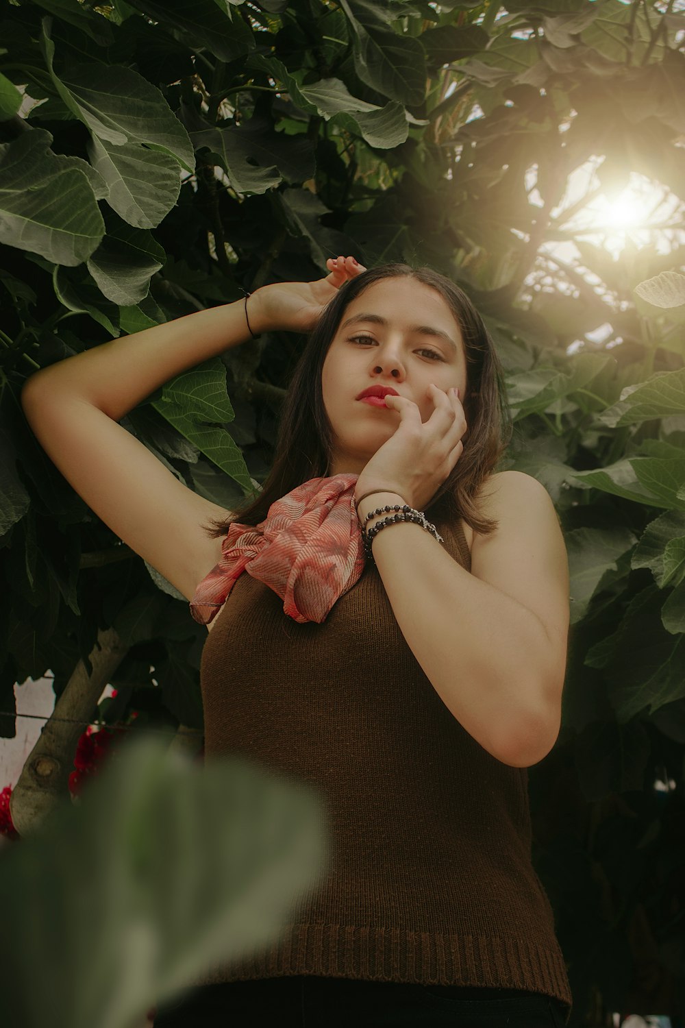 Mujer con vestido rojo sin mangas de pie junto a hojas verdes