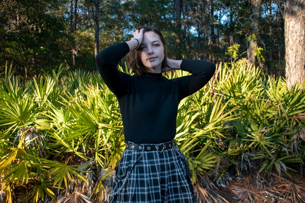 woman in black long sleeve shirt and blue and white plaid skirt standing on green grass