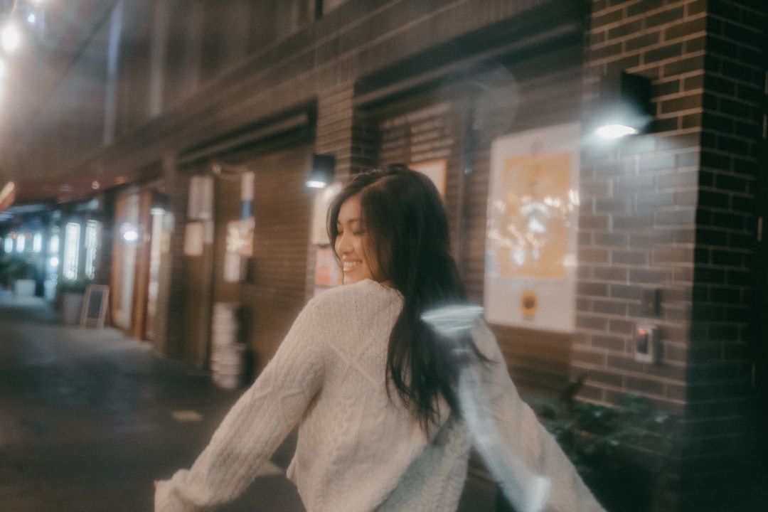 woman in white sweater sitting on the sidewalk during night time