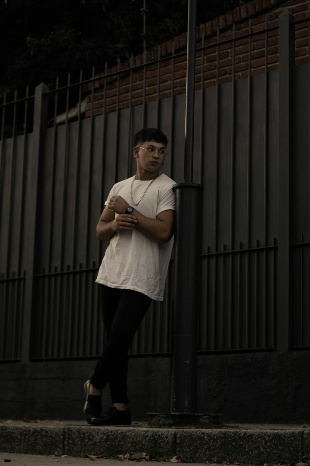 man in white crew neck t-shirt and black pants standing beside gray steel gate during